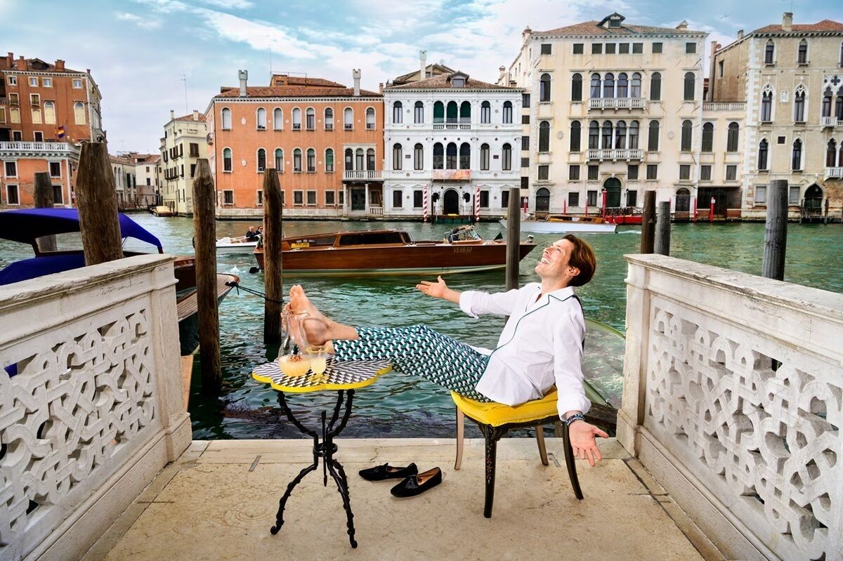 A person relaxing on a chair by a canal with buildings in the background.