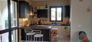 A kitchen with a central island, bar stools, a window with a view, and built-in cabinets. - Villa Thalassa, for a perfect stay, 500 meters from the sea (Fontane Bianche)