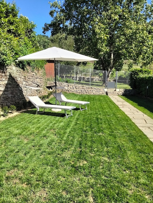 Ein gepflegter Rasen mit zwei weißen Liegestühlen und einem großen Sonnenschirm.