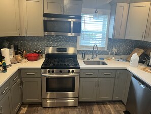 A modern kitchen with stainless steel appliances, a large window with blinds, and a tiled backsplash.