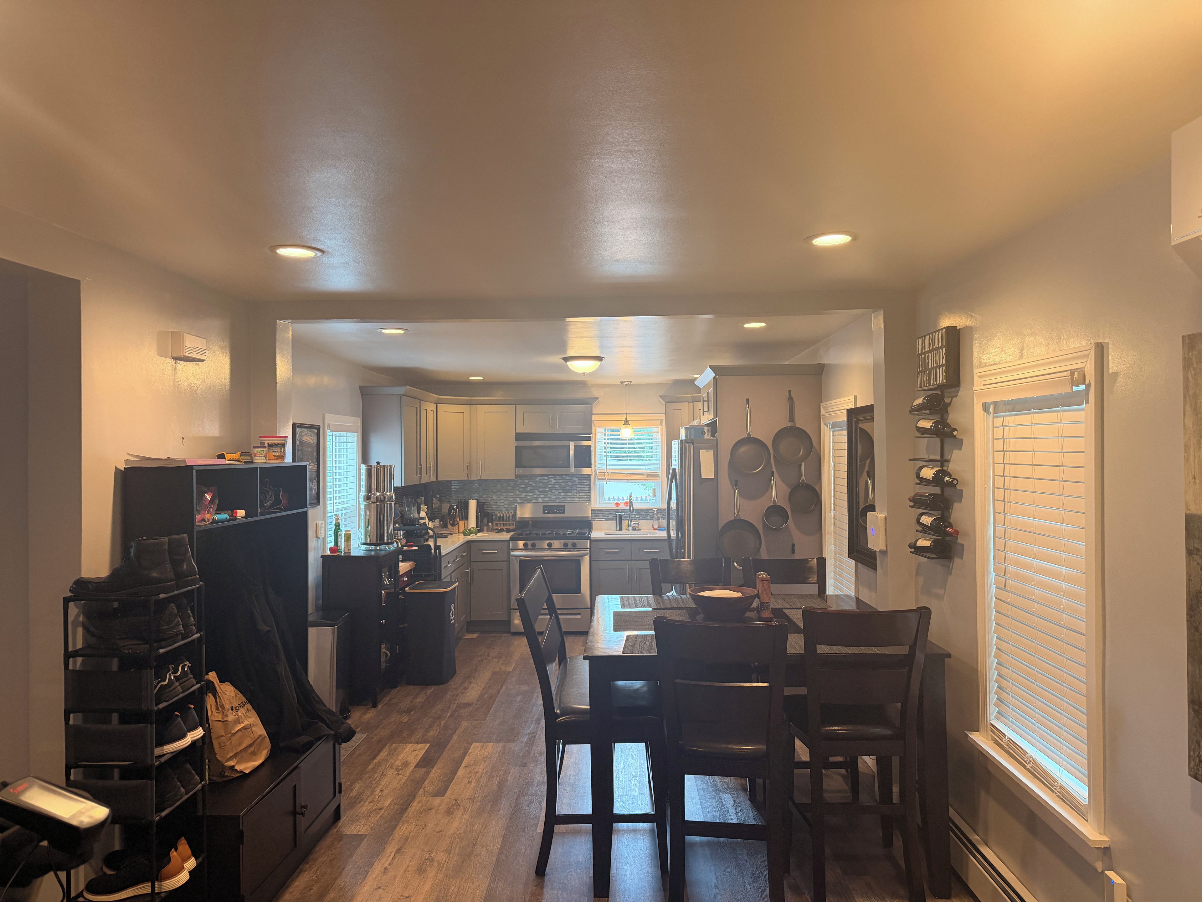 A kitchen with a dining area, wooden flooring, and a window with blinds.