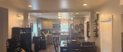 A kitchen with a dining area, wooden flooring, and a window with blinds.