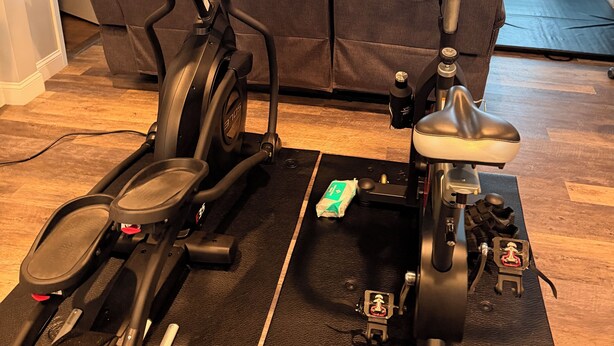 Un espace intérieur aménagé pour faire de l’exercice, avec deux vélos d’appartement, un canapé et un téléviseur en arrière-plan.