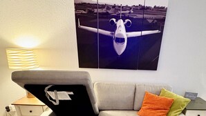 Ein Sofa mit Stauraum, eine Lampe und ein gerahmtes Bild eines Flugzeugs an der Wand.