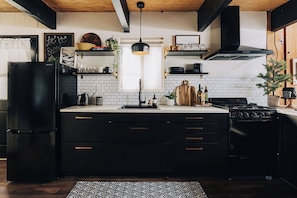 A modern kitchen with black appliances, white tiles, and wooden accents. - Firefly Cabin (Big Bear Lake)