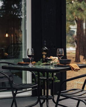 An outdoor dining area with a table set for two, featuring a bottle of Cuppola wine, two glasses, bread, and a bowl. - Firefly Cabin (Big Bear Lake)