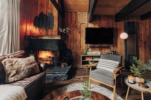 A cozy living room with a fireplace, a television, and a comfortable seating area. - Firefly Cabin (Big Bear Lake)