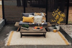 A wooden bench with cushions, a woven rug, a table with a fruit bowl, and potted plants. - Firefly Cabin (Big Bear Lake)