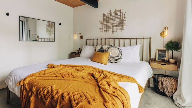 A bedroom with a large bed, a bedside table, a wall-mounted light, and a decorative wall piece. - Firefly Cabin (Big Bear Lake)