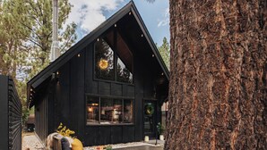 A cabin with a sloped roof, large windows, and a wooden deck with outdoor seating. - Firefly Cabin (Big Bear Lake)