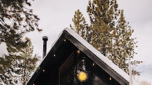 A cabin with a sloped roof, large windows, and a wreath on the door. - Firefly Cabin (Big Bear Lake)