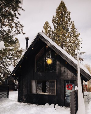 A cabin with a sloped roof, large windows, and a wreath on the door. - Firefly Cabin (Big Bear Lake)