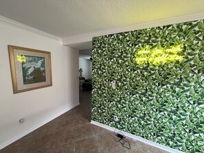 Ein Flur mit einem gerahmten Kunstwerk, einer Neonreklame und einer Wand mit einem Blattmuster.