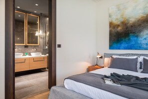 Een moderne hotelkamer met een groot bed, een nachtkastje met een lamp, een badkamer met spiegel en wastafel, en een groot abstract schilderij aan de muur.