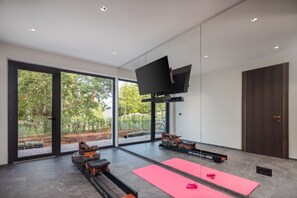 Een moderne kamer met een groot raam, trainingsapparatuur, een flatscreentelevisie en een deur.