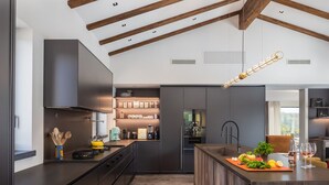 A modern kitchen with dark cabinetry, a central island, and a hanging light fixture. - Villa Cypress Hill, Spacious 4-bedroom estate  with Spa,  fitness & tennis court (Rakotule)