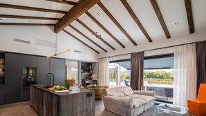 Eine moderne Küche mit einer zentralen Kochinsel, einem Essbereich mit einer Couch und einem großen Fenster mit Vorhängen.