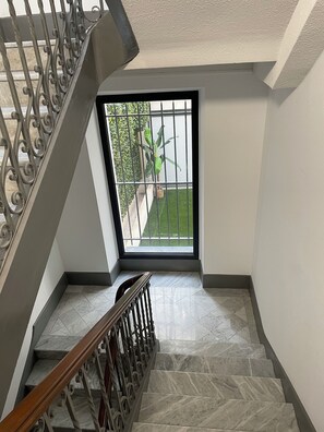 Eine Treppe mit Marmorstufen und einem Holnlauf, die zu einem Balkon mit Blick auf einen Garten und ein Gebäude führt.