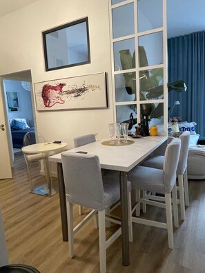 Ein moderner Essbereich mit einem weißen Tisch, grau gepolsterten Stühlen und einem großen Fenster mit Blick auf einen blauen Himmel.