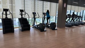 Un gimnasio con diferentes máquinas de cardio, ventanas amplias y suelo de madera.