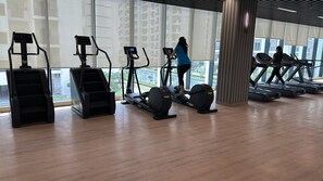 Ett gym med olika typer av konditionsmaskiner, stora fönster och ett trägolv.
