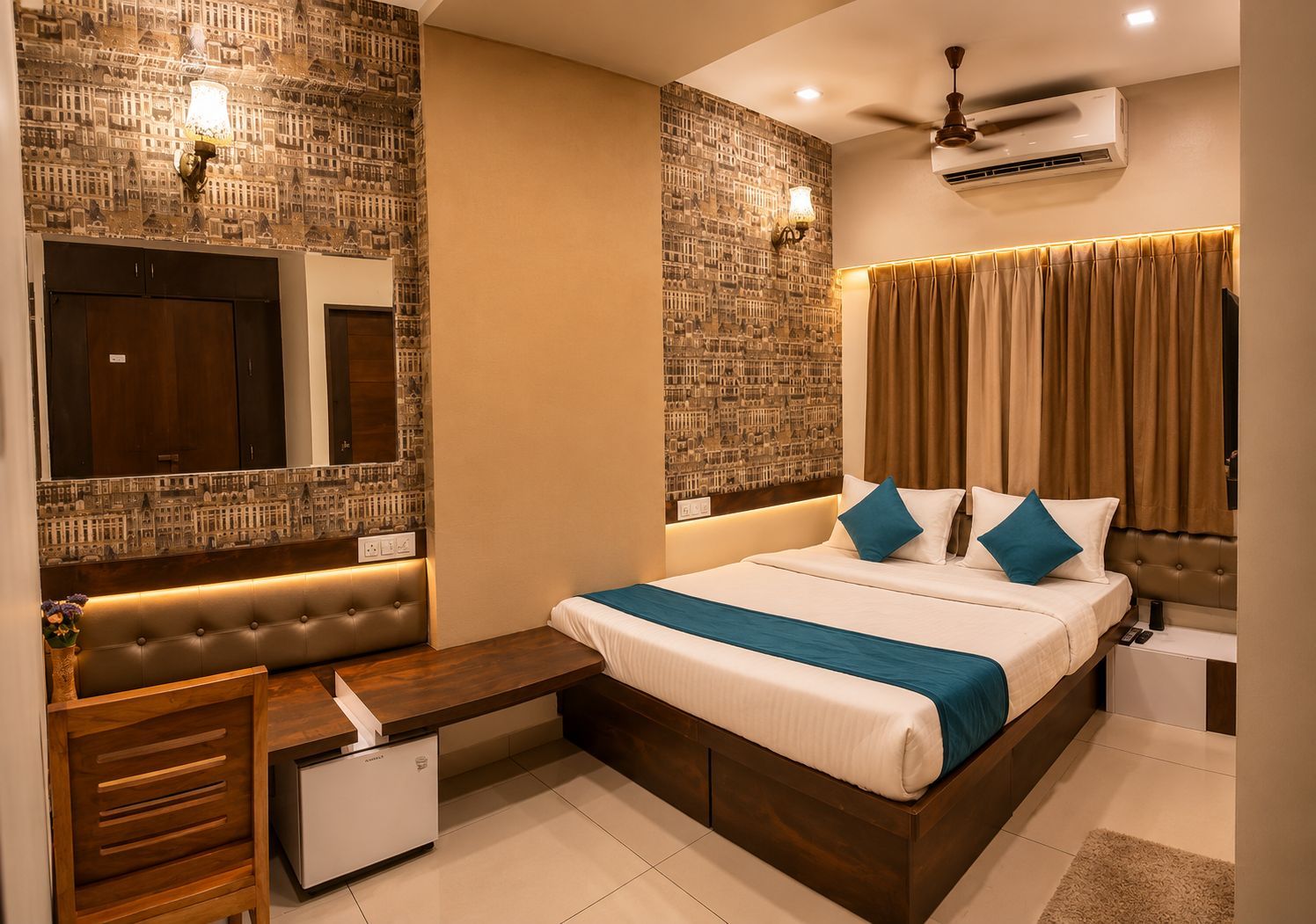 A hotel room with a large bed, a vanity with a mirror, a small desk, a ceiling fan, and an air conditioning unit.
