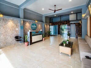 A hotel reception area with a reception desk, seating, potted plants, and a ceiling fan. - Kubo By Convivial Hotels (Indore)