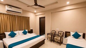 Habitación de hotel con dos camas, ventilador de techo, unidad de aire acondicionado, una puerta y dos sillas.