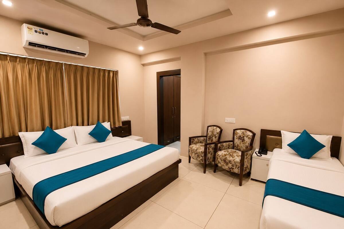 A hotel room with two beds, a ceiling fan, an air conditioning unit, a door, and two chairs.