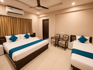 Habitación de hotel con dos camas, ventilador de techo, unidad de aire acondicionado, una puerta y dos sillas.