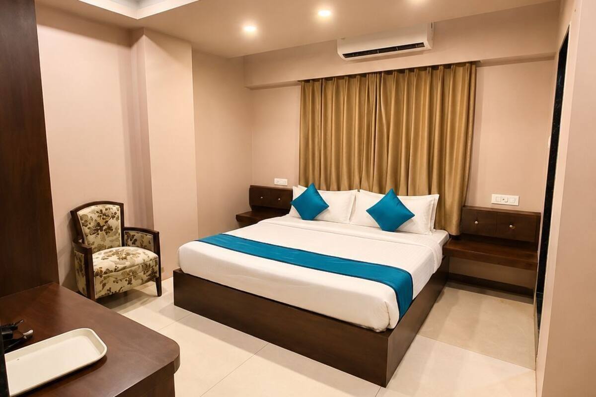 A hotel room with a bed, bedside tables, a chair, a desk, and an air conditioning unit.