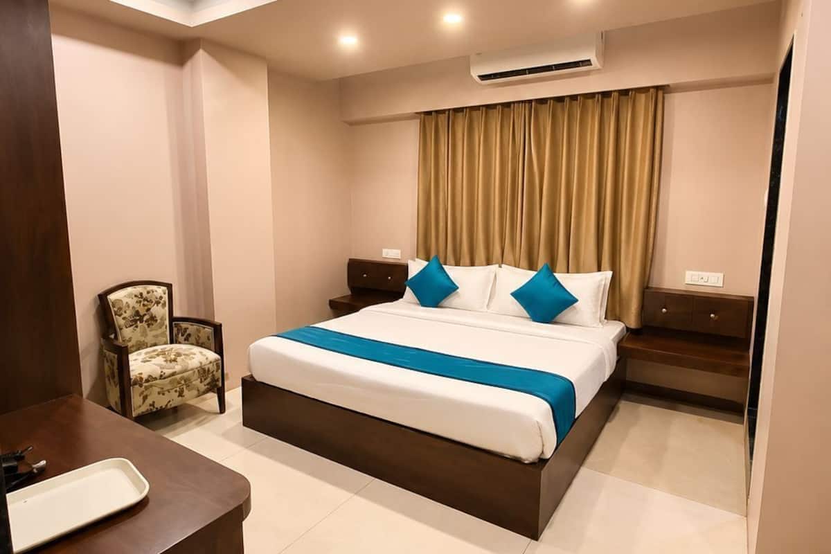 A hotel room with a bed, bedside tables, a chair, a desk, and an air conditioning unit.