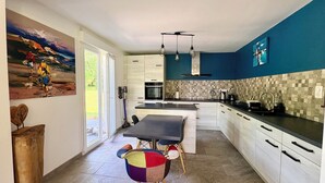 A modern kitchen with a dining area, large windows, and a colorful abstract painting.