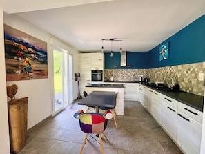 Une cuisine moderne avec un coin repas, de grandes fenêtres et un tableau abstrait aux couleurs vives.