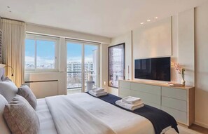 Ein modernes Hotelzimmer mit einem großen Bett, einem Flachbildfernseher, Blick auf die Stadt und einem minimalistischen Design.