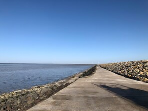 A coastal walkway with a stone wall, a concrete path, and wind turbines in the distance. - Gîte Mer et Marais at Soleil Levant (Bouin)