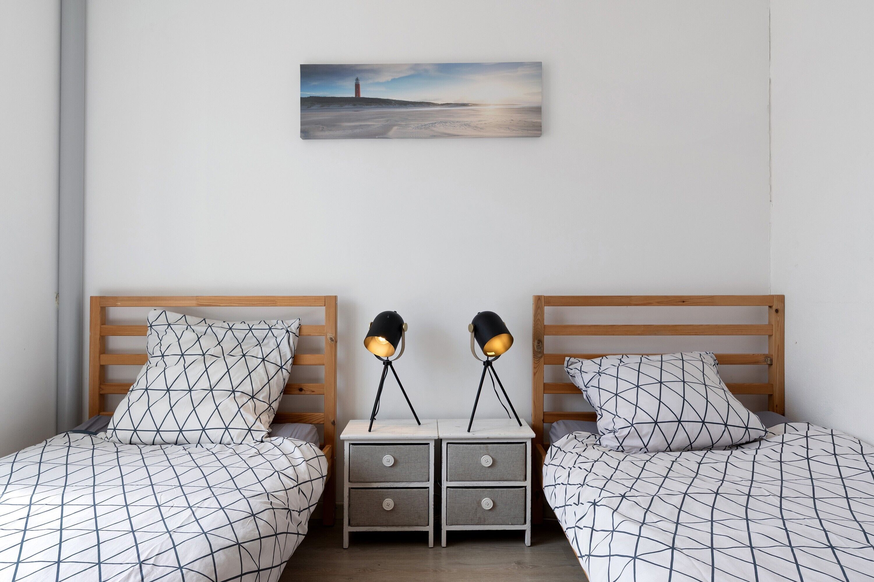 Ein Schlafzimmer mit zwei Betten, einem Nachttisch mit Schubladen, zwei Nachttischlampen und einem Gemälde an der Wand.