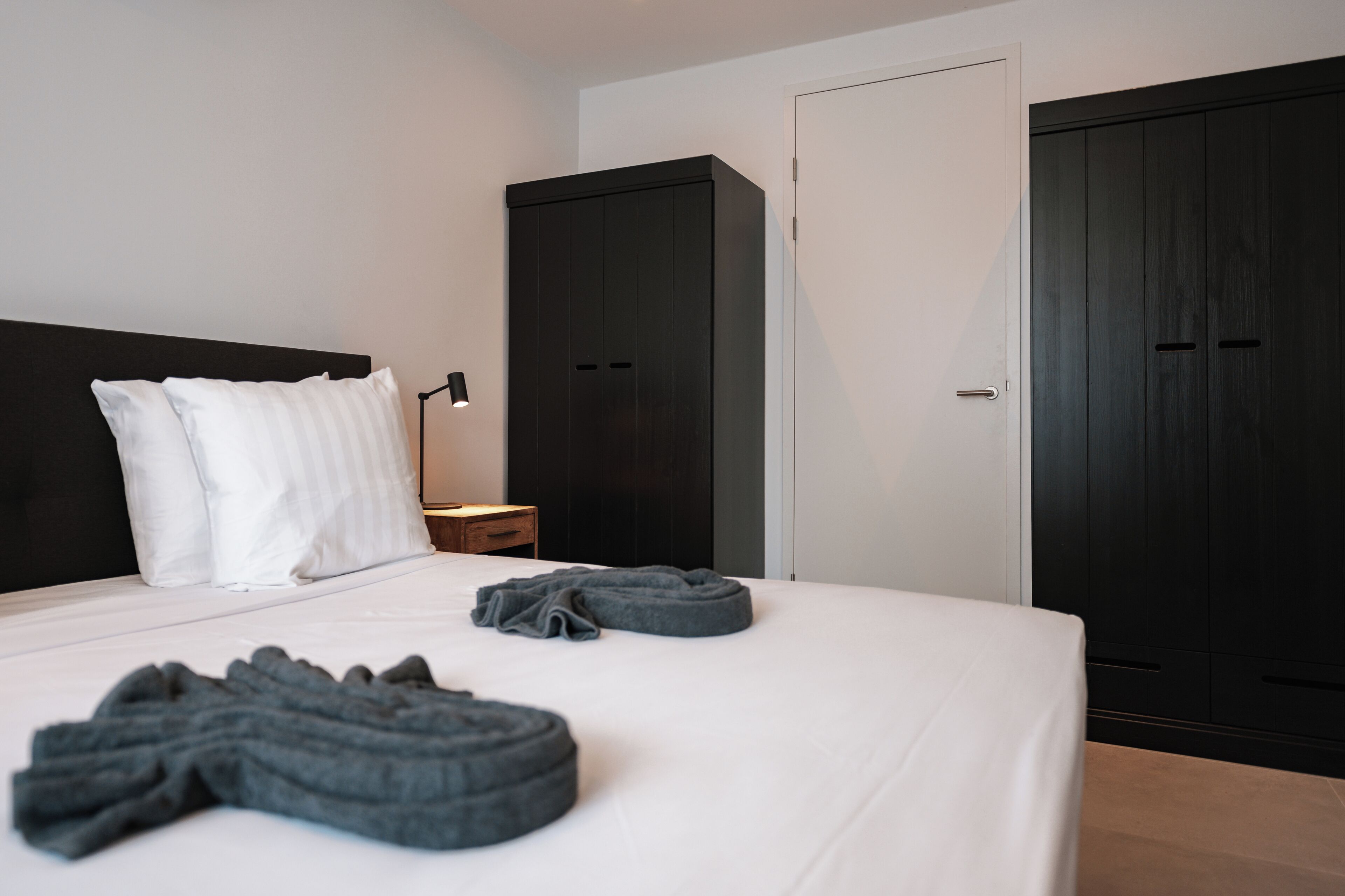 Une chambre d’hôtel avec un lit, deux armoires sombres, une table de chevet et une lampe.