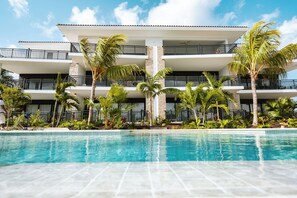 Ett hotell med flera våningar, en swimmingpool, palmer och en klarblå himmel.