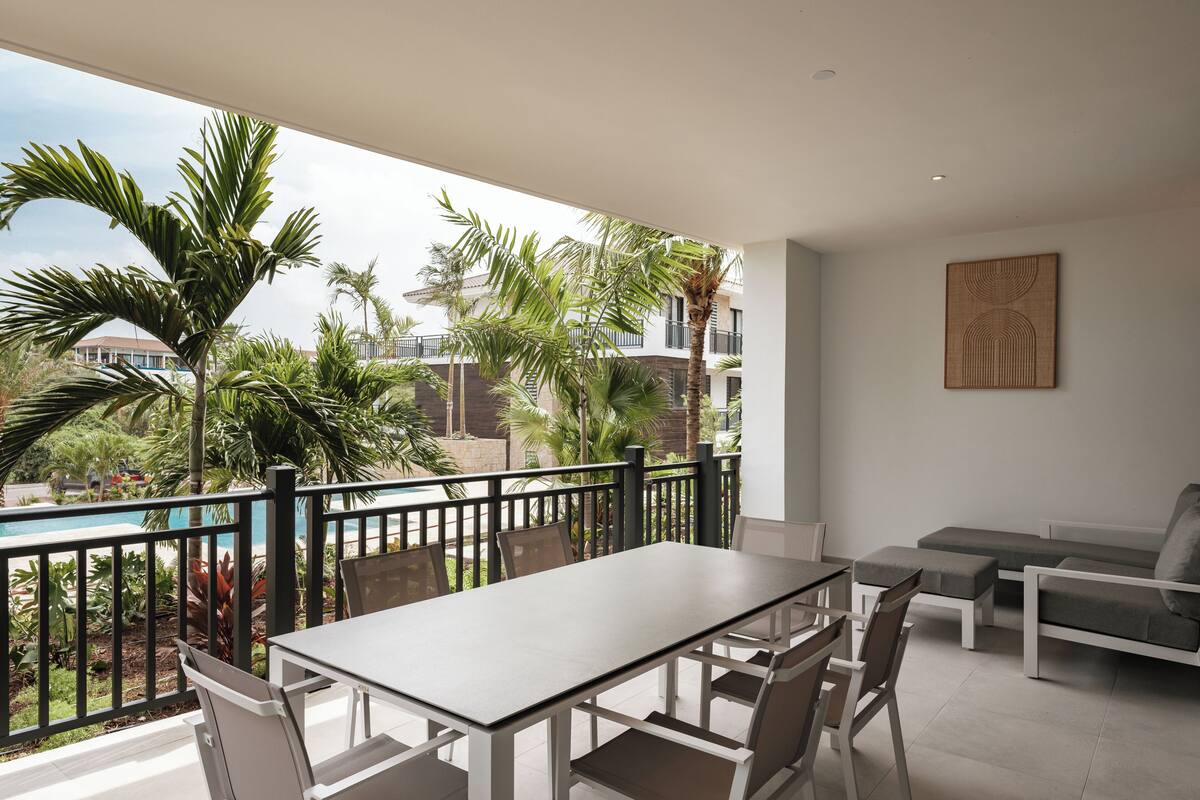 Un balcón con mesa y sillas, un sofá y vistas a palmeras y edificios.