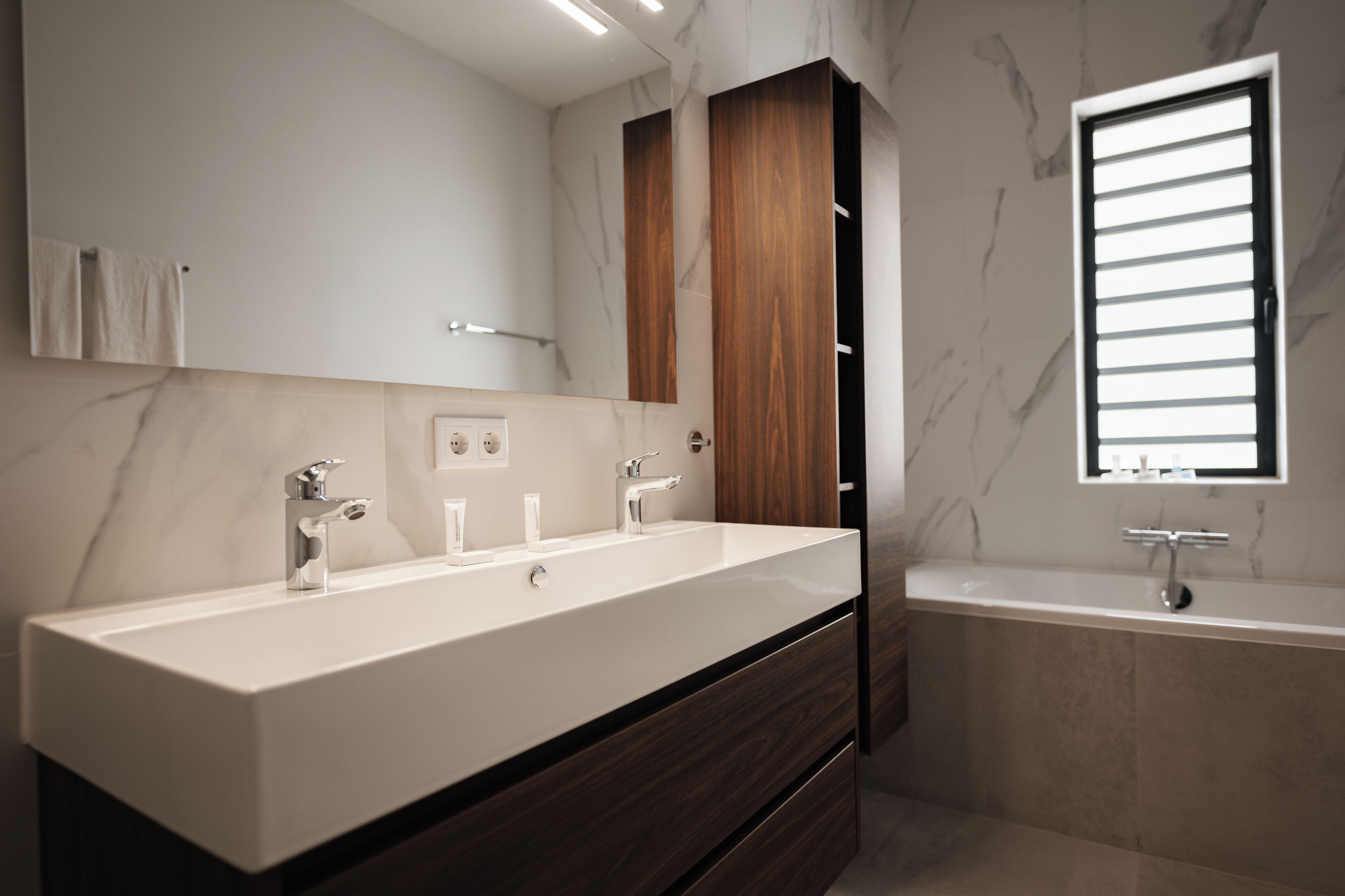 Ein modernes Badezimmer mit einem großen Waschbecken, einem Spiegel und einem Fenster.