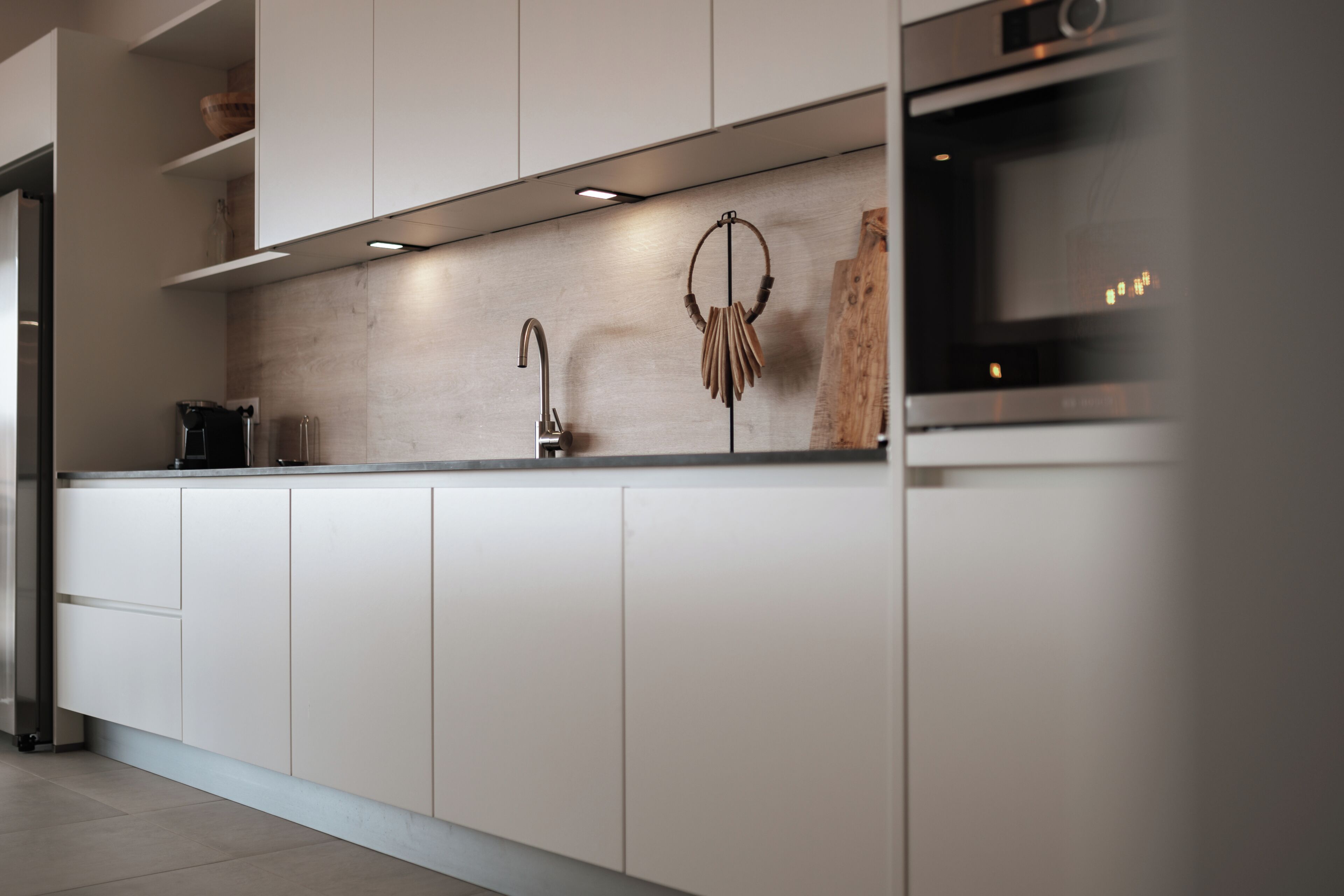 A modern kitchen with white cabinetry, a stainless steel sink, and a built-in oven.