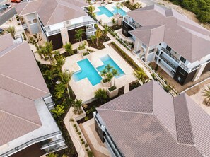 A resort with multiple buildings, a central swimming pool, and surrounding greenery. - The Breeze -Blue Bay Golf & Beach Resort (Sint Michiel)