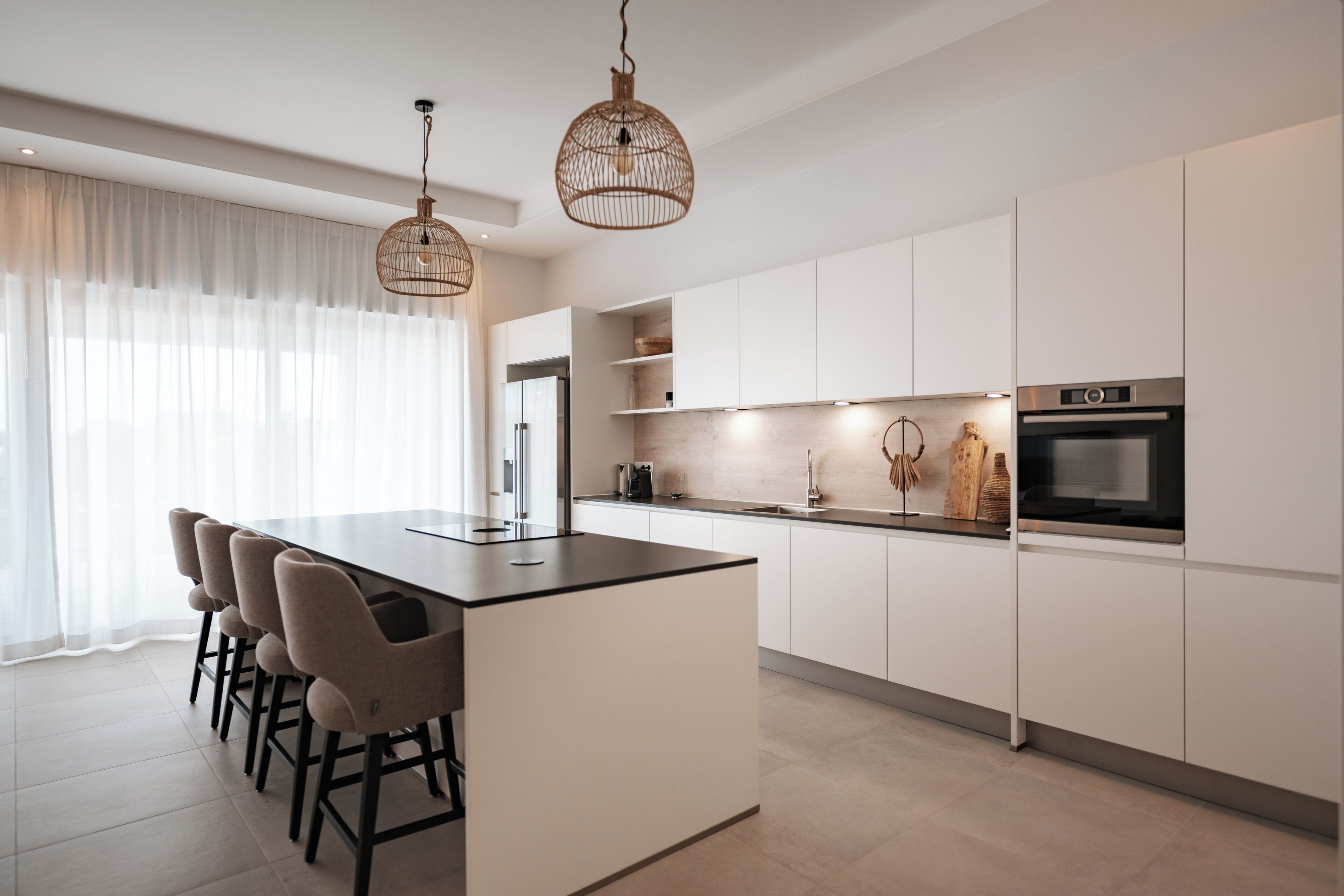 Una cocina moderna con una isla central, taburetes de bar, iluminación colgante y electrodomésticos integrados.