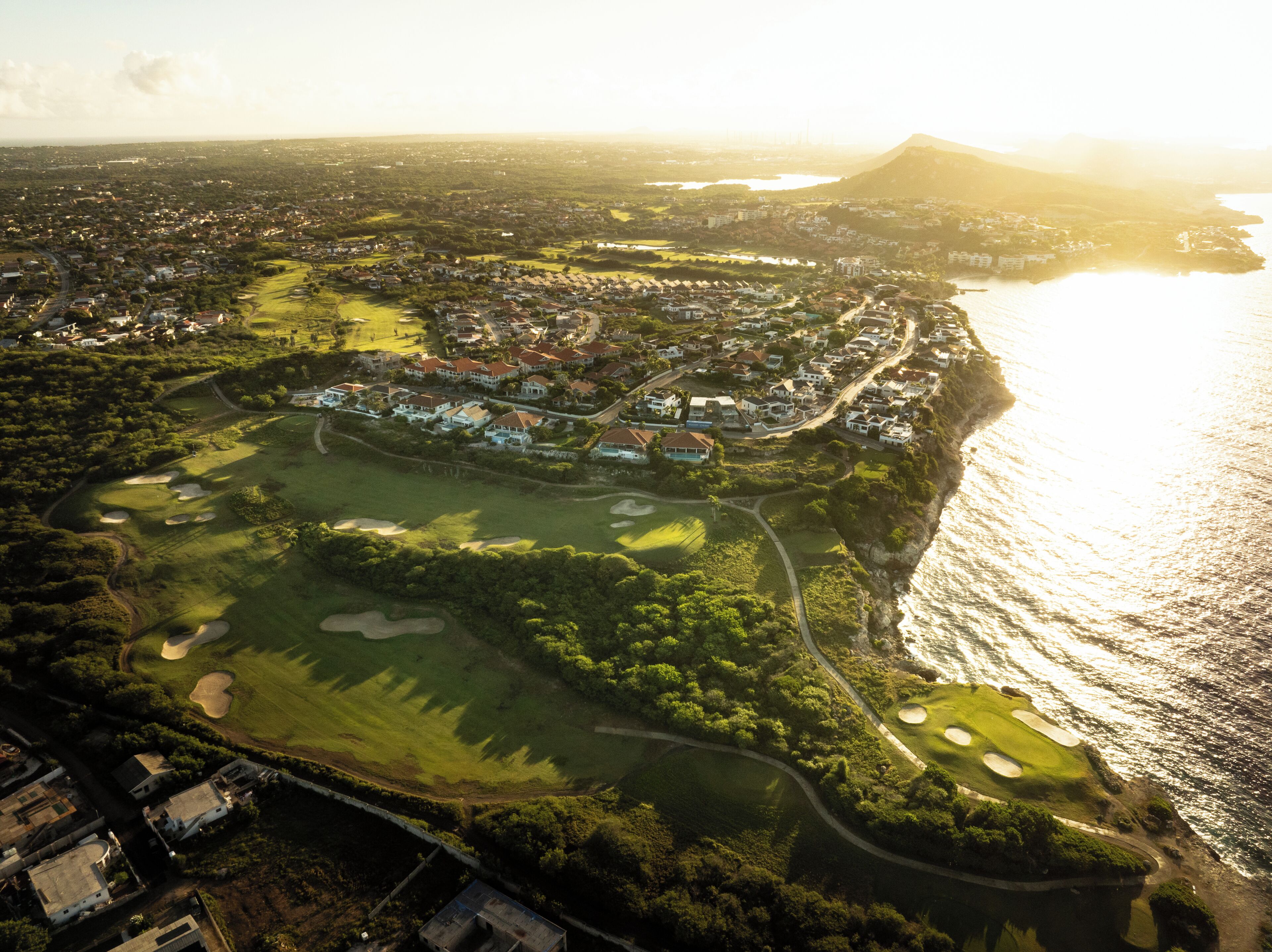 An aerial view of a coastal town with a golf course, residential areas, and a mountain in the background.