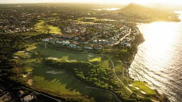 An aerial view of a coastal town with a golf course, residential areas, and a mountain in the background.