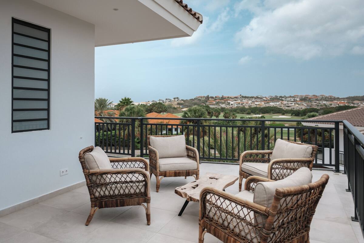 Un balcón con mobiliario de mimbre y vista a una zona residencial.