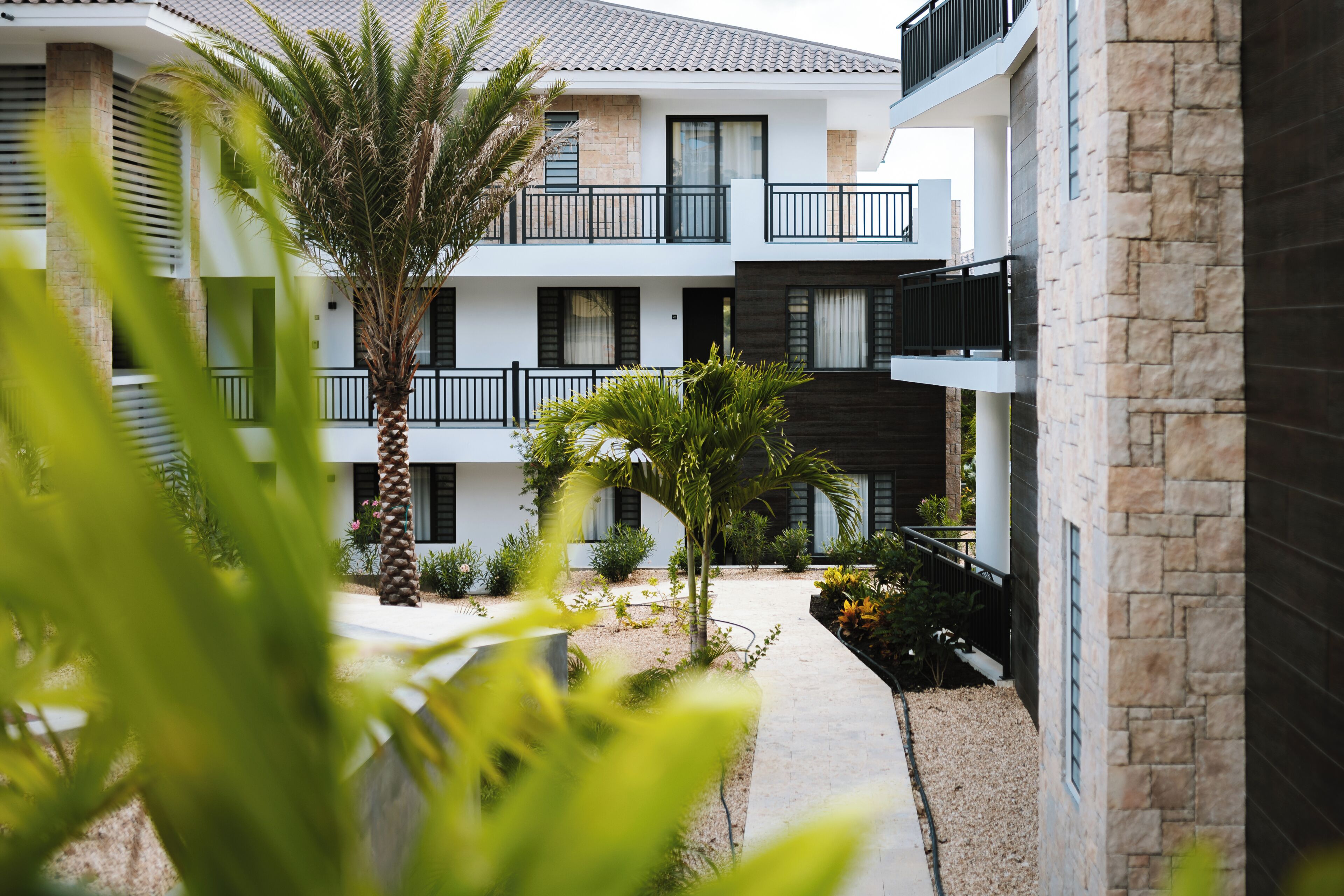 A modern multi-story building with balconies, a central courtyard with plants, and a stone facade.