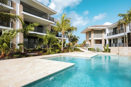 A resort with a swimming pool, multiple balconies, and palm trees.. The Breeze -Blue Bay Golf & Beach Resort