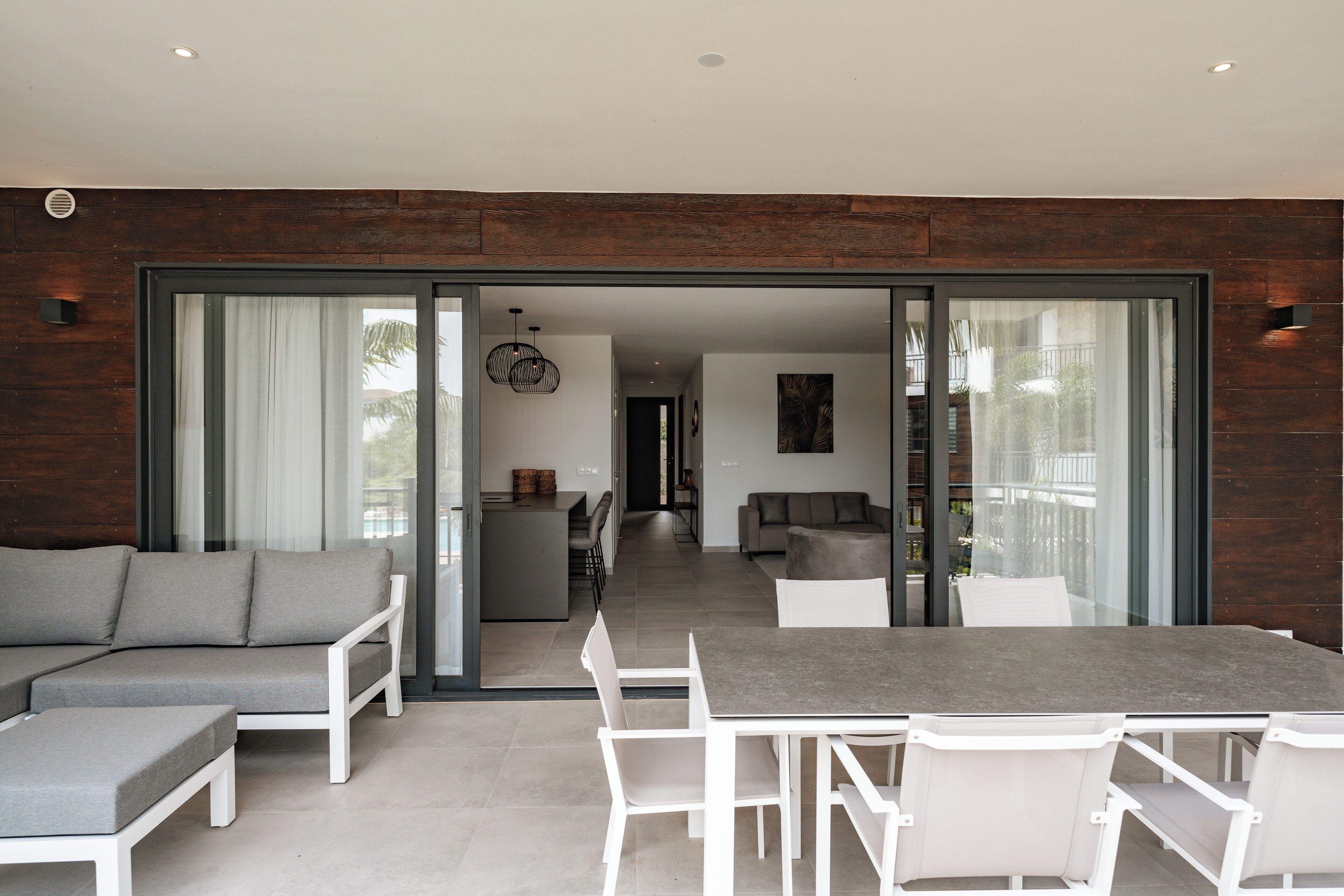An open-plan living area with a dining table, white chairs, a grey sofa, and a kitchen in the background.